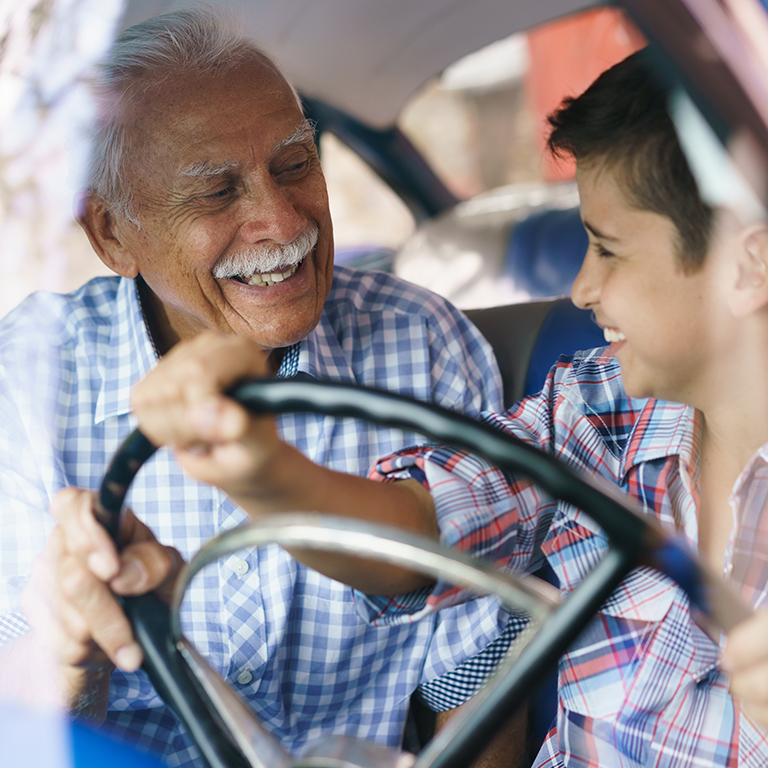 older man and young boy holding steering wheel in car
